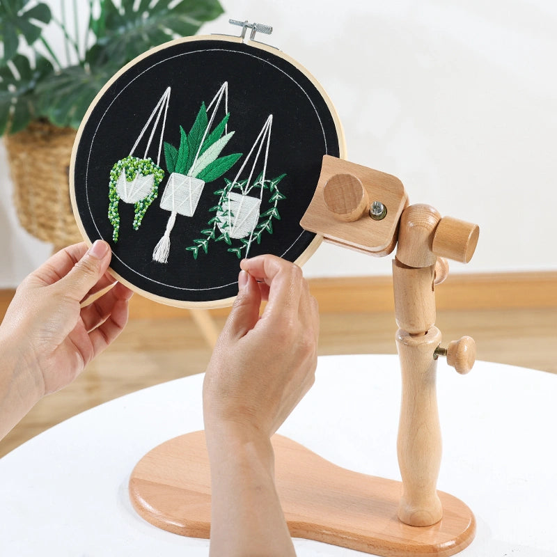 Embroidery hoop with plant-themed design held by a person on a wooden stand.