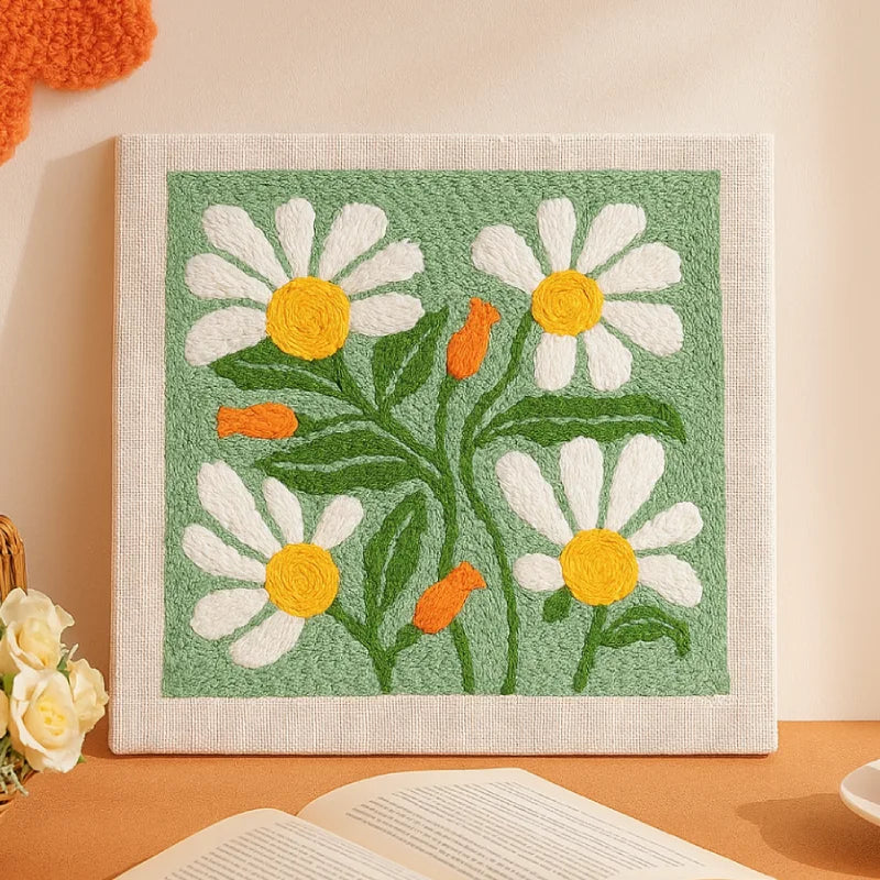 This punch needle artwork features bright white daisies with cheerful yellow centers and soft orange buds set against a fresh green background. 