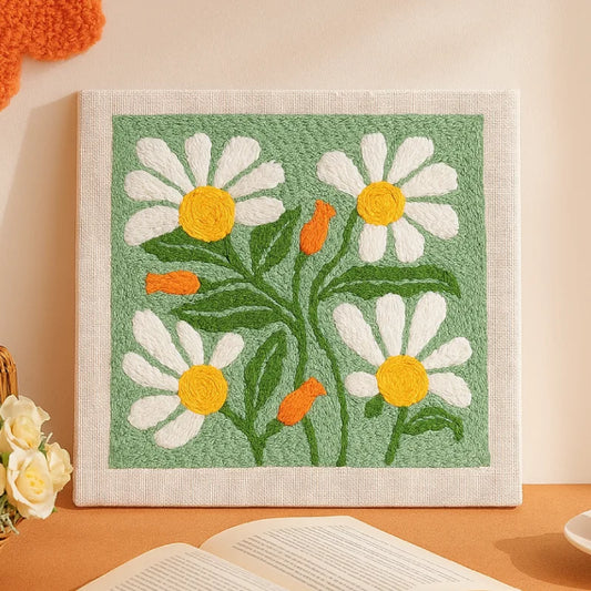 This punch needle artwork features bright white daisies with cheerful yellow centers and soft orange buds set against a fresh green background. 