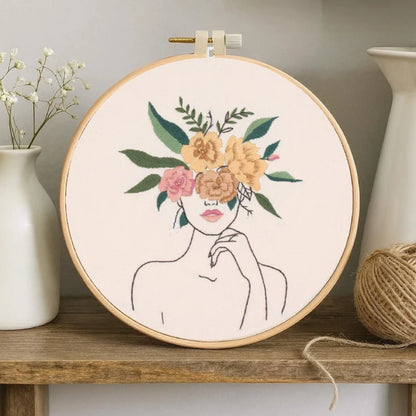 This embroidery design, titled Blooming Grace, features the elegant outline of a woman with her eyes veiled by blooming flowers. The gentle blend of pink and golden blooms with lush green leaves symbolizes the harmony between nature and feminine beauty — calm, confident, and effortlessly graceful.