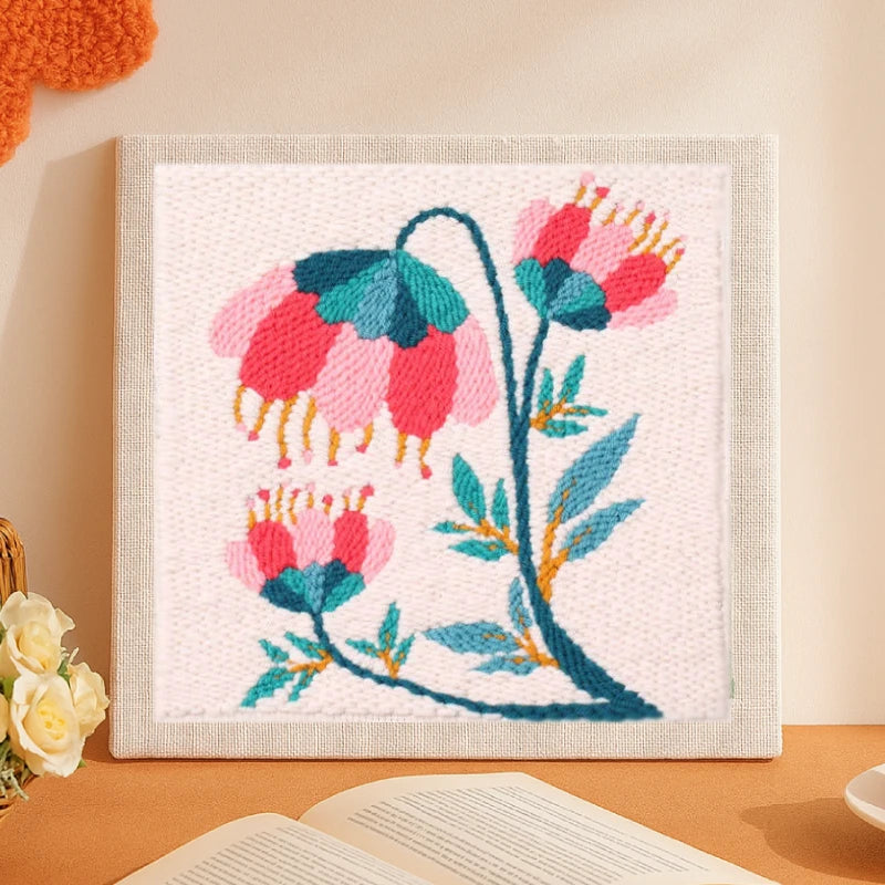 This elegant punch needle piece depicts graceful pink and teal flowers swaying on curved green stems, accented with golden details.