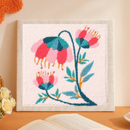 This elegant punch needle piece depicts graceful pink and teal flowers swaying on curved green stems, accented with golden details.