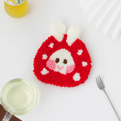 Crocheted red and white animal coaster on a white surface with a glass and fork.