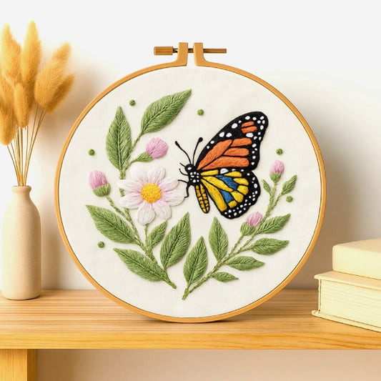 This charming embroidery design features a vibrant butterfly resting on a delicate daisy, surrounded by soft green leaves and tiny pink buds. The contrast of the butterfly’s bright orange, yellow, and blue wings brings a lively touch to the natural simplicity of the flowers. A perfect piece for home décor, adding freshness, warmth, and artistic elegance to your space.