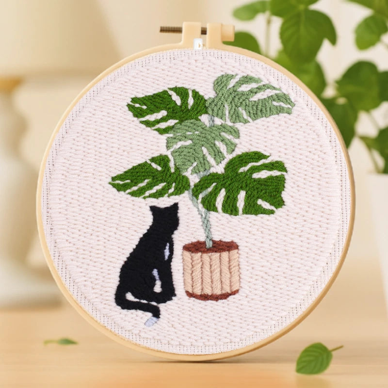 Calm Cat Punch Needles Kit — A peaceful black cat sits quietly beside a large monstera plant in a wooden pot. The lush green leaves and soft background create a calm and cozy scene. Simple and elegant, this design is perfect for beginners looking to enjoy a slow, relaxing crafting experience.