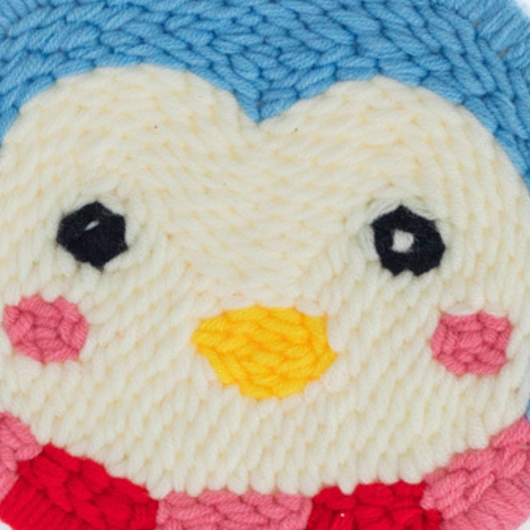 Close-up of a knitted or crocheted heart with a face, eyes, and a yellow beak on a blue background.