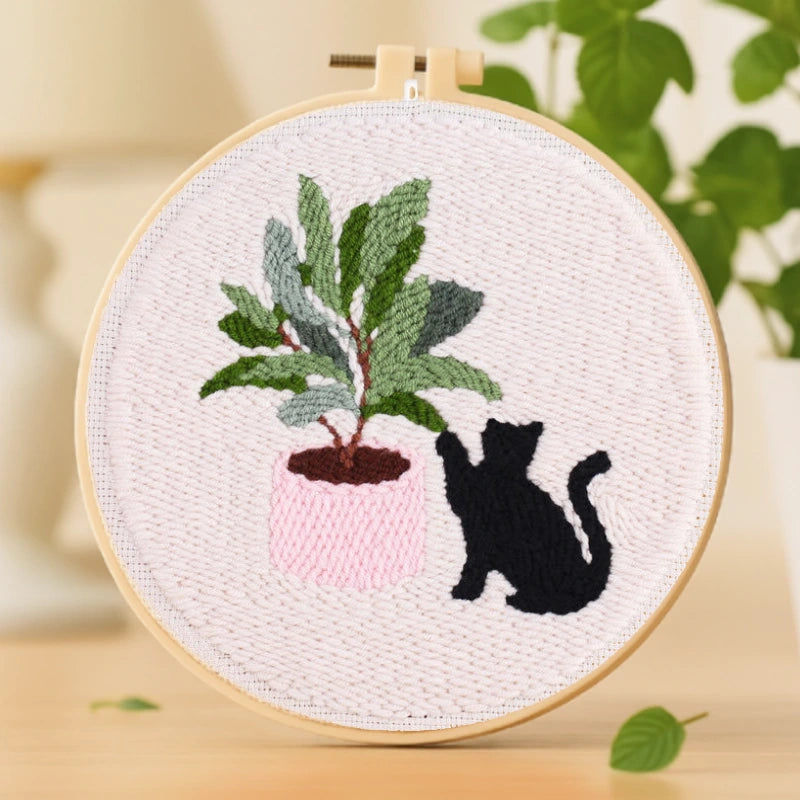 Curious Cat Punch Needle Kit — A playful little black cat curiously reaching toward a potted plant. The soft pink pot and green leaves create a lovely contrast, making the design warm and lively. Simple yet full of charm, this embroidery is perfect for beginners to enjoy a cozy handcrafting time.