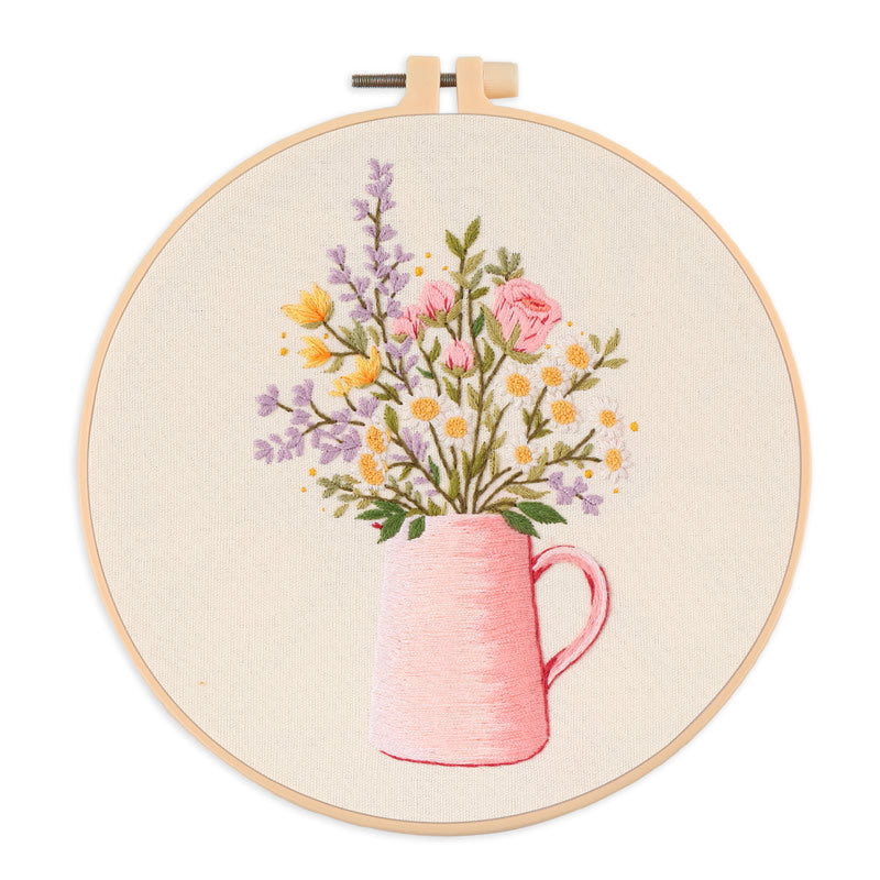 Embroidery hoop with a floral design of a pink mug and flowers on beige fabric.