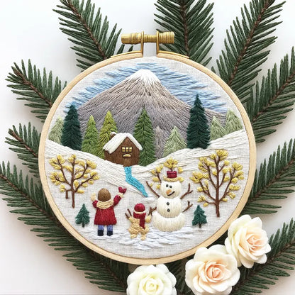 Embroidery hoop with a winter scene featuring a mountain, trees, and people, surrounded by pine branches and flowers.