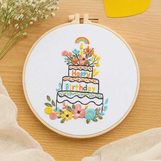 Embroidery hoop with a colorful birthday cake design on a wooden surface.