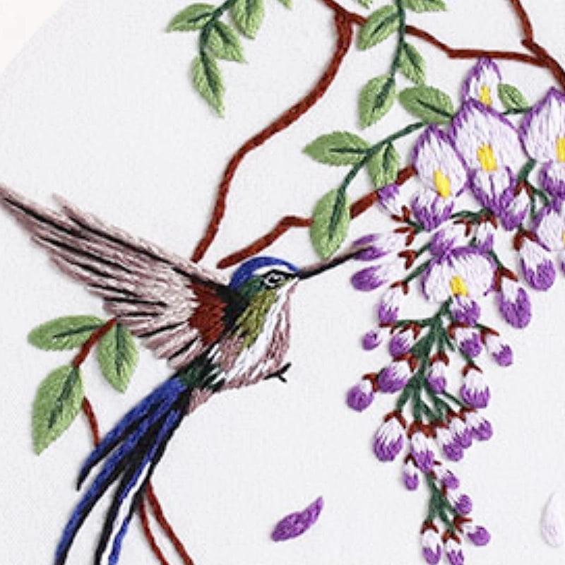 Embroidery of a hummingbird and purple flowers on a white background