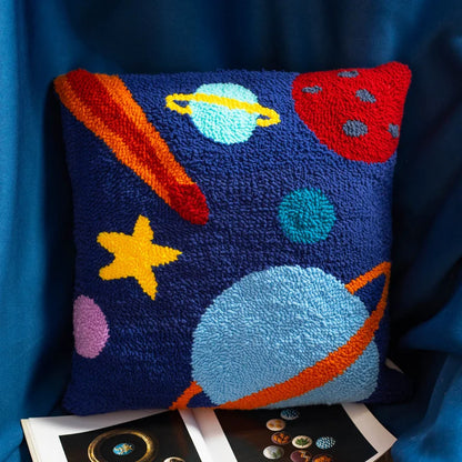 A vibrant punch needle pillow featuring colorful planets and stars floating across a deep blue sky.