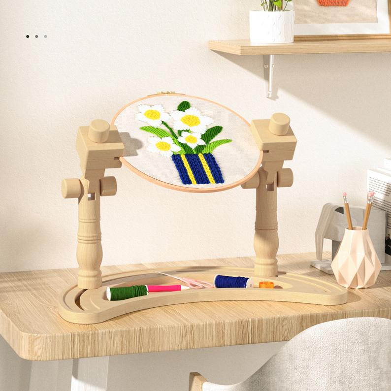 Wooden embroidery hoop with floral design on a stand on a wooden table.