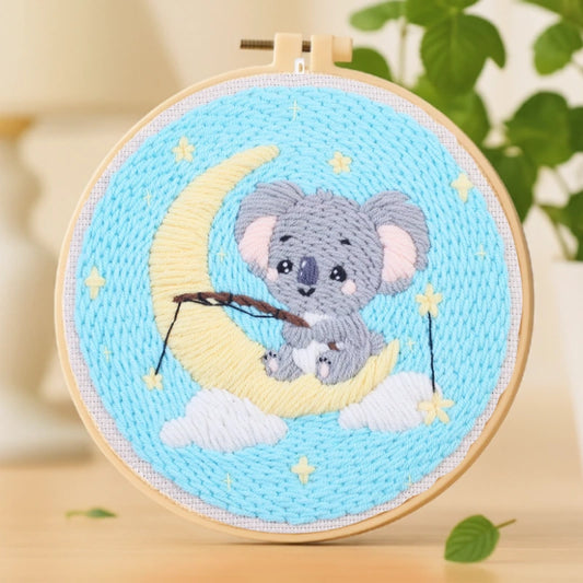 This adorable embroidery design features a cute koala sitting on a crescent moon, holding a fishing rod among twinkling stars. The soft pastel colors of blue, yellow, and gray create a dreamy night-time atmosphere.