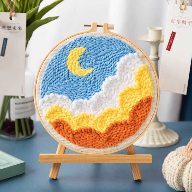 Knitted wall art with a moon and cloud design on a wooden stand.