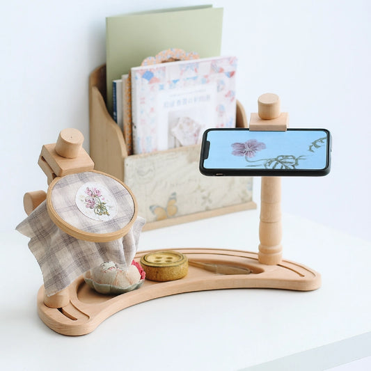 Colorful butterfly brooch on a light gray fabric background with embroidery hoop and threads.