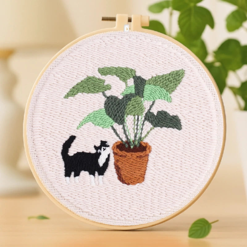 Playful Cat Punch Needles Kit — A cute black-and-white cat playfully exploring a lush green plant in a brown pot. The contrast between the greenery and the soft background creates a calm yet cheerful vibe. Simple and beginner-friendly, this design is perfect for relaxing weekend stitching or sharing with friends.
