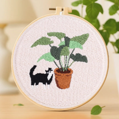Playful Cat Punch Needles Kit — A cute black-and-white cat playfully exploring a lush green plant in a brown pot. The contrast between the greenery and the soft background creates a calm yet cheerful vibe. Simple and beginner-friendly, this design is perfect for relaxing weekend stitching or sharing with friends.