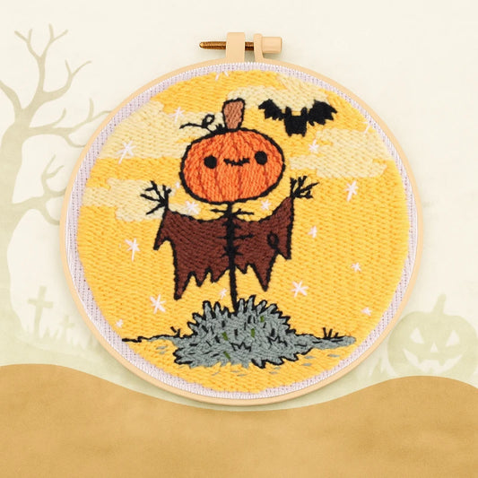 This punch needle design features a cheerful pumpkin-headed scarecrow under a golden Halloween sky, with a playful bat flying nearby.