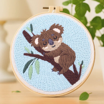 This cozy embroidery design shows an adorable koala peacefully napping on a tree branch. The soft shades of brown and green, set against a light blue background, create a calm and soothing feeling. Perfect for beginners, it’s a delightful piece to relax with on weekends or to gift someone who loves cute, heartwarming designs.