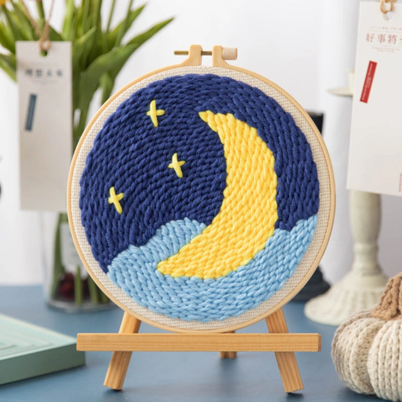 Woven circular art piece with a moon and stars design on a wooden stand.