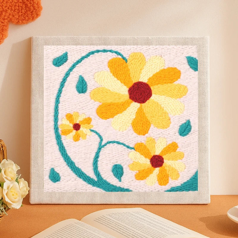 This lovely punch needle artwork features three bright golden-yellow flowers with deep red centers and curved teal stems and leaves dancing gracefully on a soft beige background. The warm, cheerful tones bring a sunny and uplifting vibe, making it a perfect piece to brighten up any cozy space.