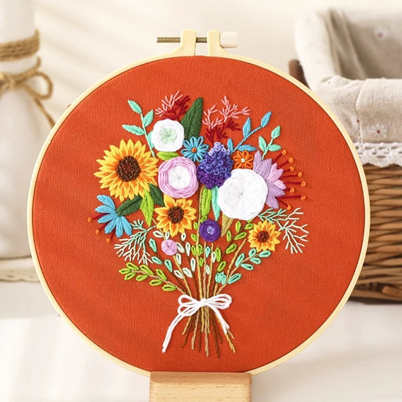 The Sunshine Bouquet embroidery design features a vibrant arrangement of flowers on a warm terracotta background.
At the centre, bright sunflowers radiate warmth and positivity, while white and purple roses add a touch of elegance and grace.
Delicate blue blossoms and green leaves weave through the bouquet, creating a lively and balanced composition.
A simple white bow ties the stems together, completing this charming display of nature’s beauty — like a bouquet freshly picked from a summer garden.