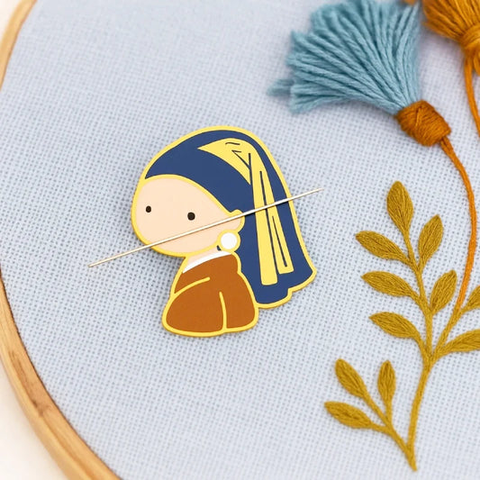 Silver tree-shaped needle holder on a fabric background with embroidery