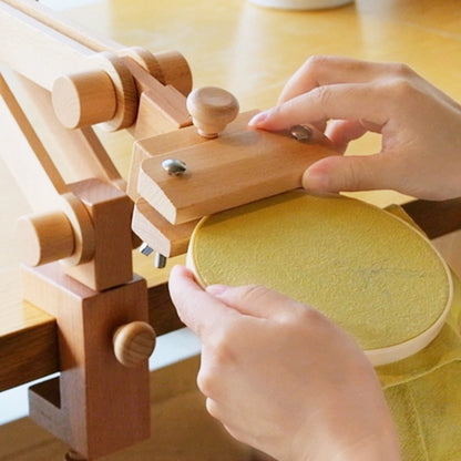 Wooden tool with a circular component being adjusted by hands on a wooden surface.
