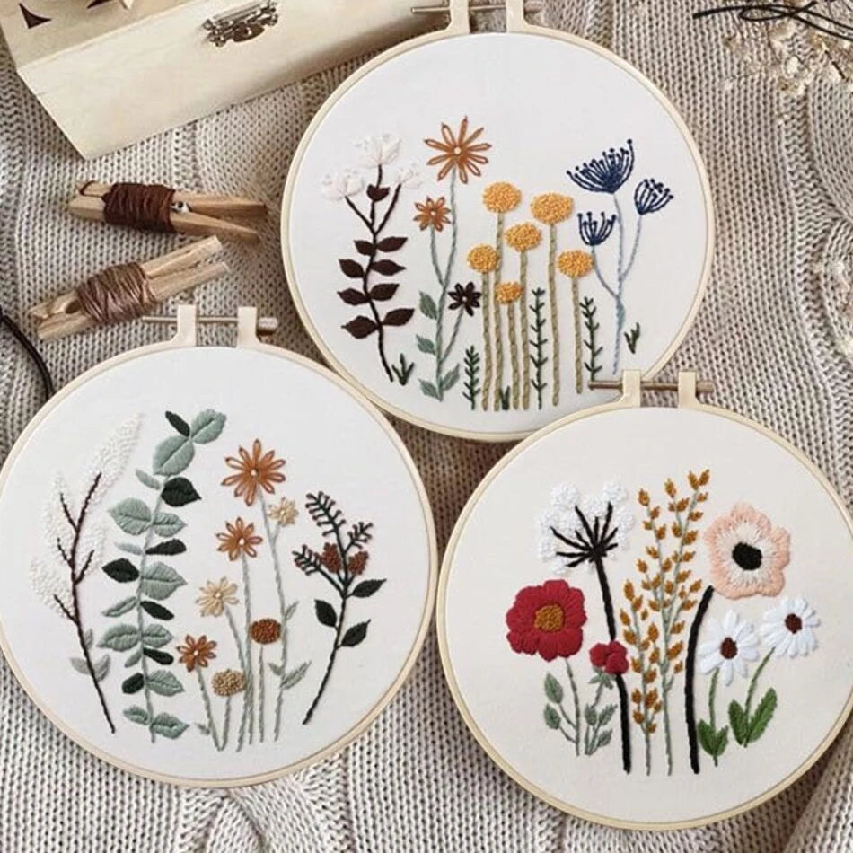 Three embroidery hoops with floral patterns on a textured fabric background