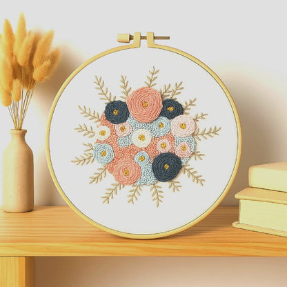 A delicate floral embroidery featuring soft pink, blue, and cream blossoms intertwined with deep navy and golden accents. The minimalist background enhances the texture and warmth of the bouquet, evoking the calm elegance of spring mornings.