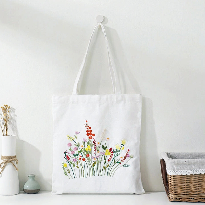 White tote bag with floral design hanging on a hook against a white wall.